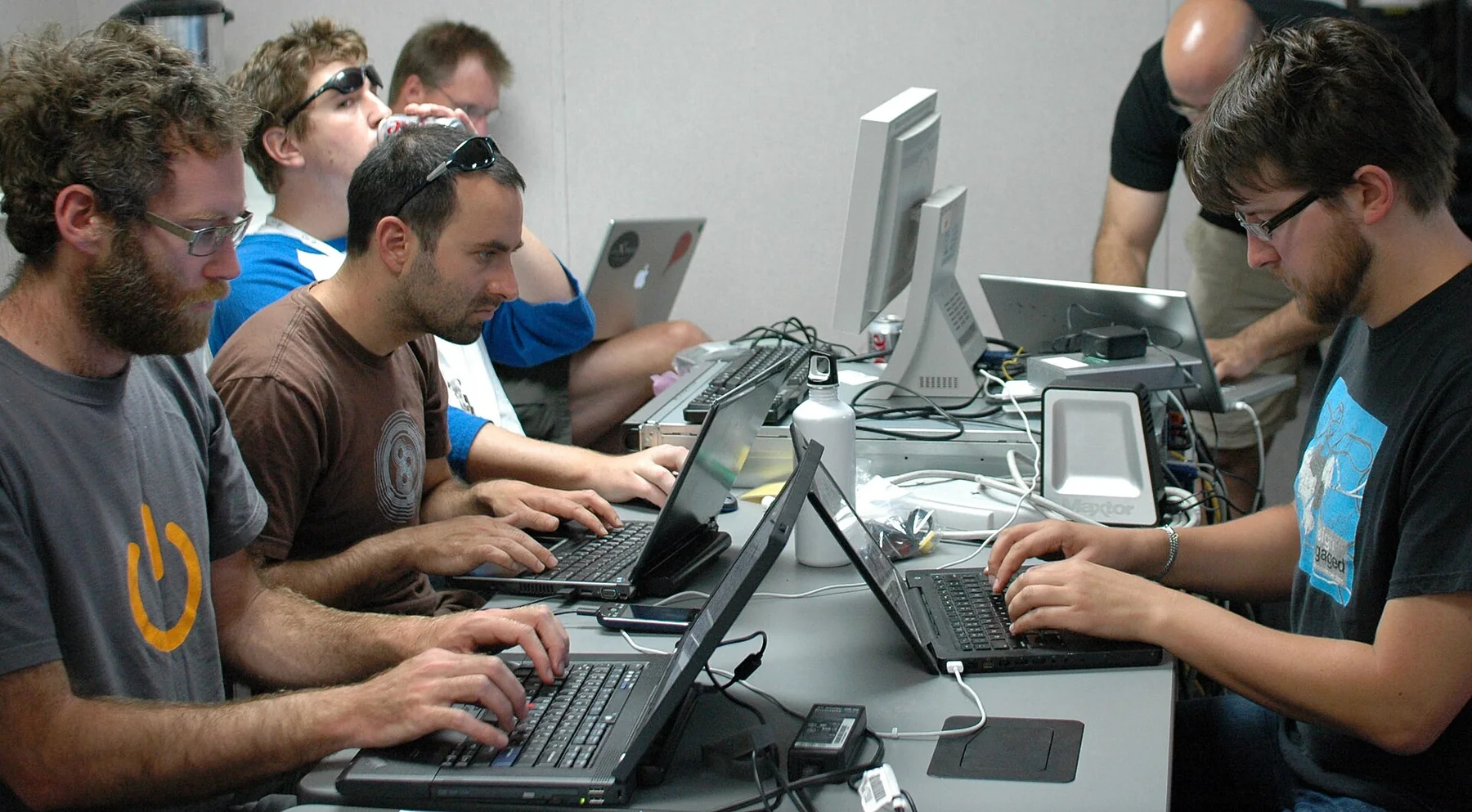 A row of people working on laptops together at a shared table during a code sprint.