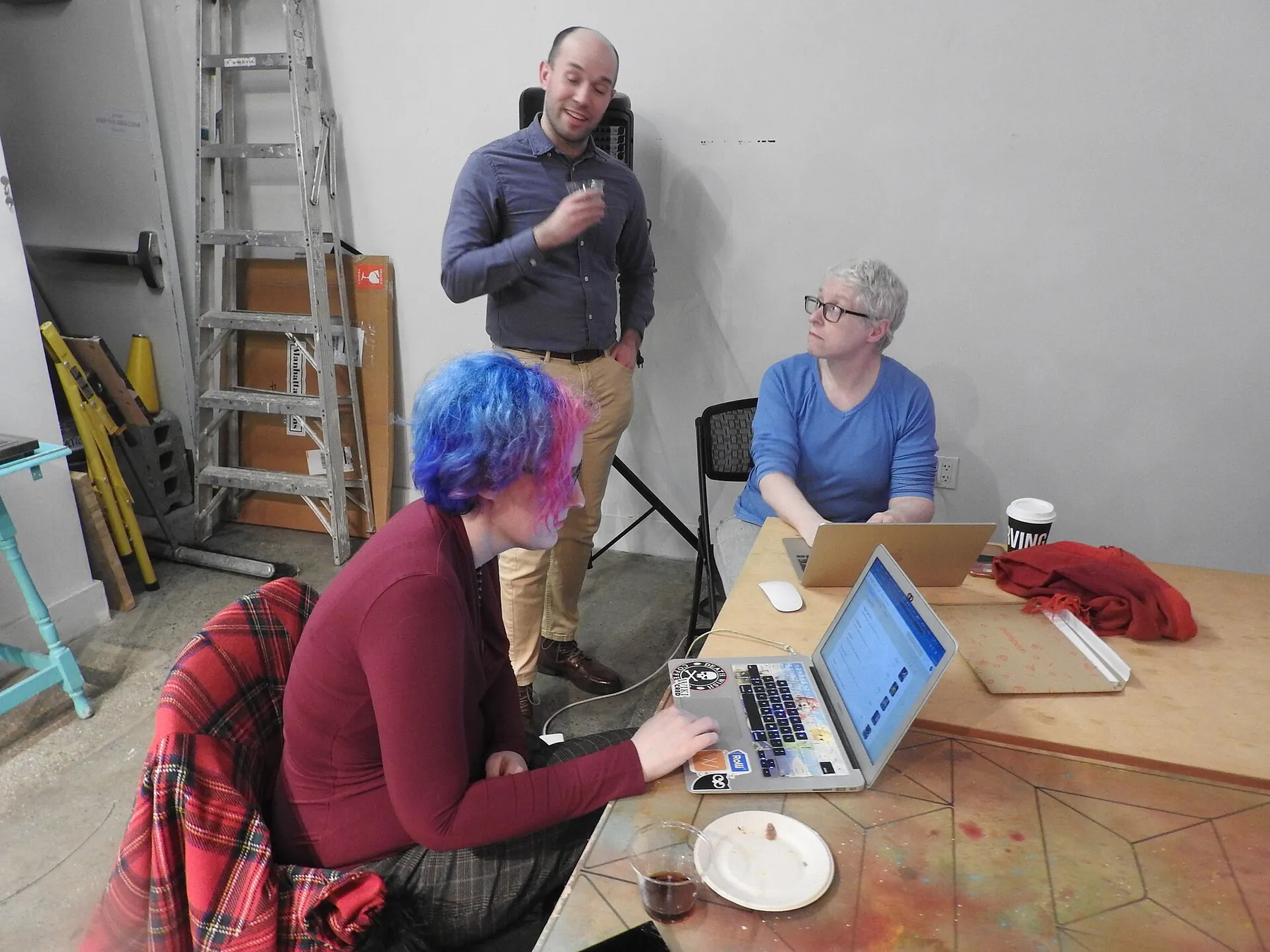 Three people working together around a table with laptops in a shared workspace.